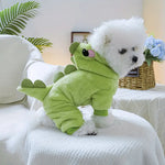 Small white dog wearing a green dinosaur costume on a white couch.