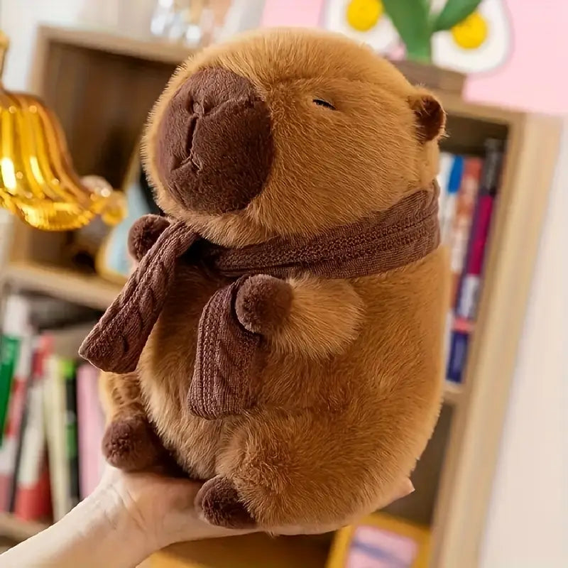 Plush toy beaver wearing a scarf held by a hand with a blurred bookshelf background