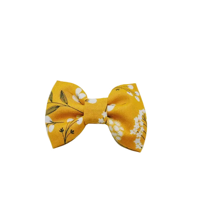 A yellow fabric bow tie featuring a white floral and black leaf pattern, photographed on a clean, white background.