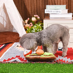 Dog playing with a toy resembling a hot dog on a blanket outdoors.