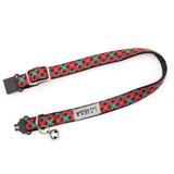 A red and green plaid pet collar with black plastic hardware, a silver metal D-ring, and a small silver bell. A fabric label on the collar reads 'WORTHY C*T'.