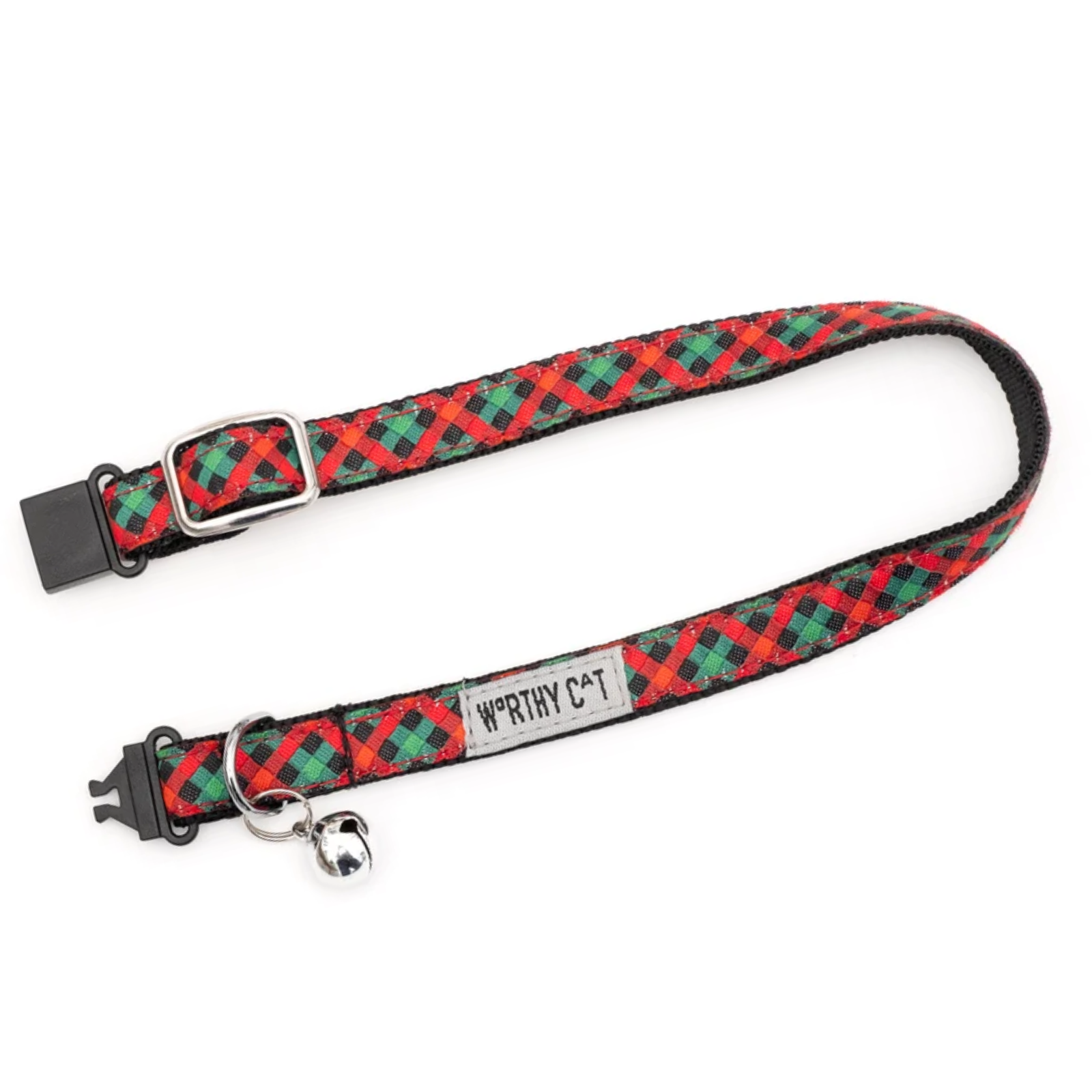 A red and green plaid pet collar with black plastic hardware, a silver metal D-ring, and a small silver bell. A fabric label on the collar reads 'WORTHY C*T'.