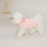 White dog wearing a pink polka dot outfit on a light background with 'Pets Tale' branding.