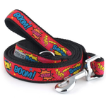 A coiled dog leash with a black woven strap and a red printed panel featuring comic-style text like BOOM!, SMASH!, and POW!, with yellow and blue graphic bursts and silver metal hardware.