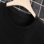 Close-up of a black crew-neck t-shirt hanging on a light wood hanger against a dark gray tiled background with a white wire grid.