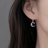 Silver moon-shaped earring worn by a person with dark hair.