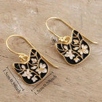 Pair of gold earrings with black and white floral designs on a wooden surface, accompanied by measurements.