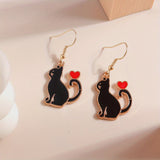 Black cat earrings with red hearts on gold hooks against a light background