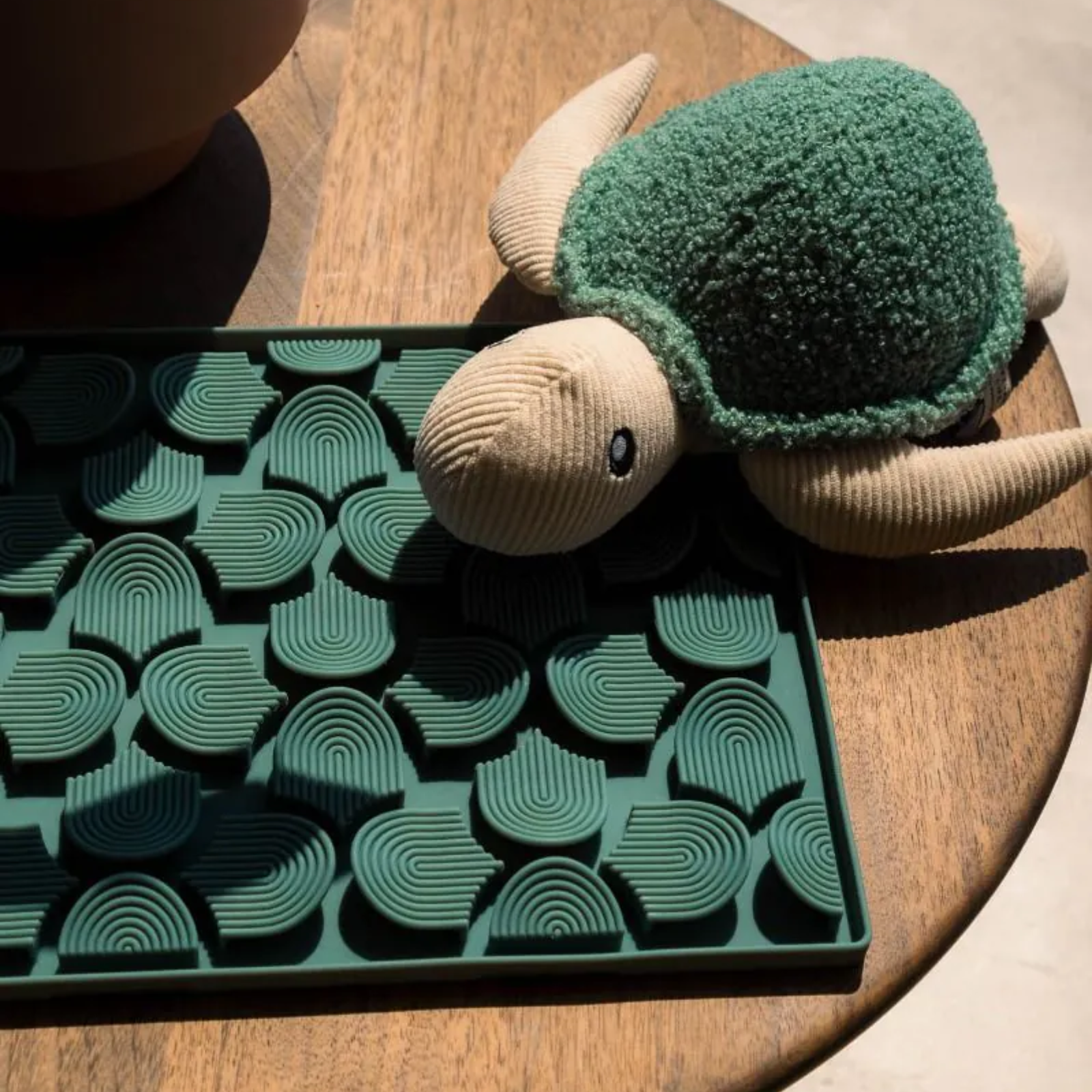 Toy turtle with green shell on a wooden surface next to a decorative tray with geometric pattern