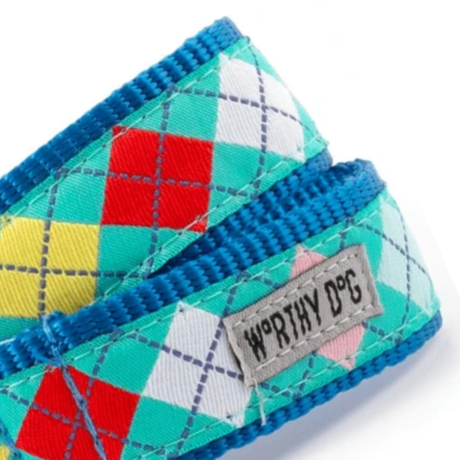 A close-up of a dog collar with a blue braided edge and an argyle pattern in teal, red, yellow, white, and pink. A gray fabric label on the collar reads 'WORTHY DOG'.