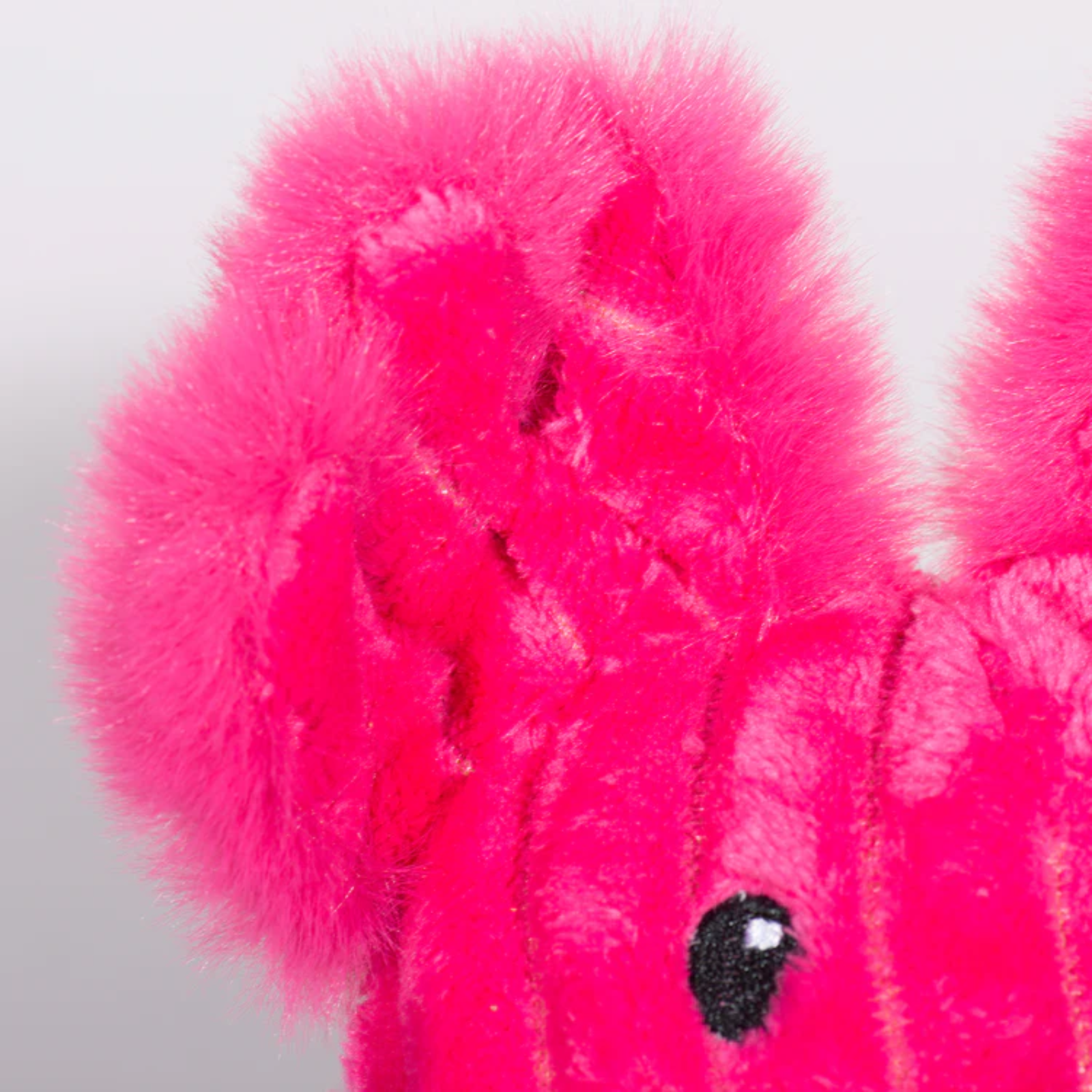 Close-up of a bright pink plush toy with black eyes on a light gray background
