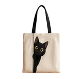 A canvas tote bag with black shoulder straps, featuring a printed illustration of a black cat peeking from behind a vertical line on the front, set against a plain white background.
