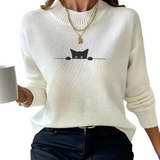 White sweater with a black cat design held by a person with a white mug.