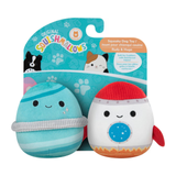 Two Squishmallows toys, one blue and one white with a red hat, in front of their packaging.