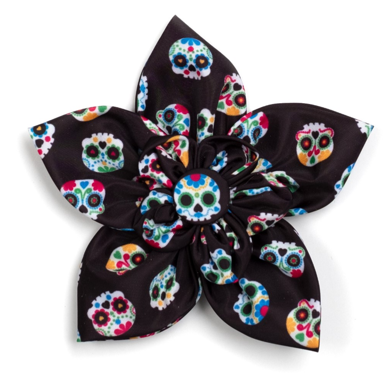 A fabric flower hair clip with a black satin-like base printed with colorful sugar skull motifs, shown on a plain white background.