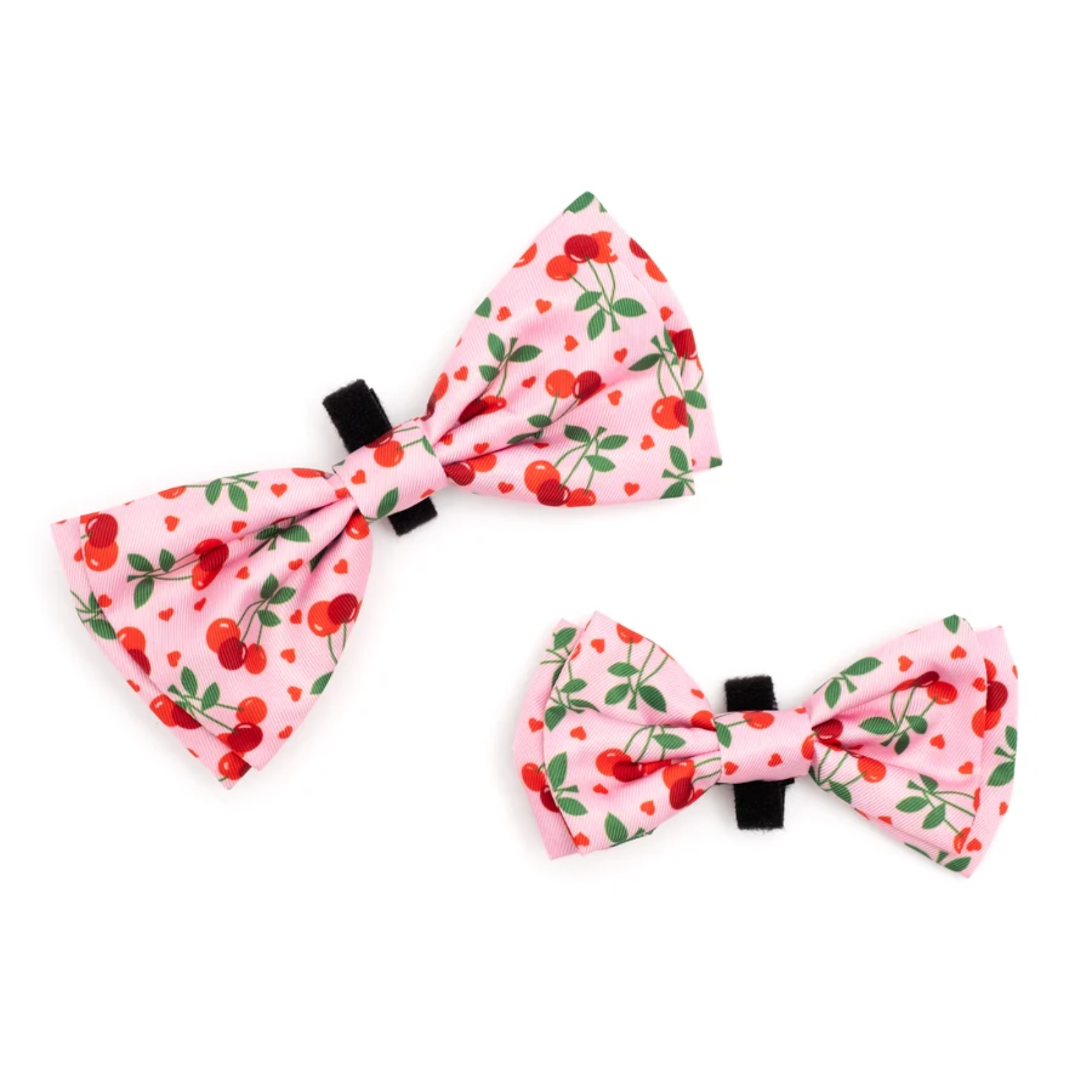 Two pink fabric bow ties with a red cherry and green leaf pattern, displayed on a clean white background.