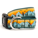 A woven dog collar with a colorful landscape print of mountains, pine trees, and a sunset. The collar features a teal green border, a silver metal D-ring, and a black plastic quick-release buckle.