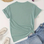Mint green t-shirt with a knot detail, paired with denim jeans and a straw hat on a light background.