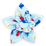 A fabric flower hair clip with six petals in light blue, featuring a pattern of red and yellow fish with small cartoon eyes, and a matching blue and white ruffled center.