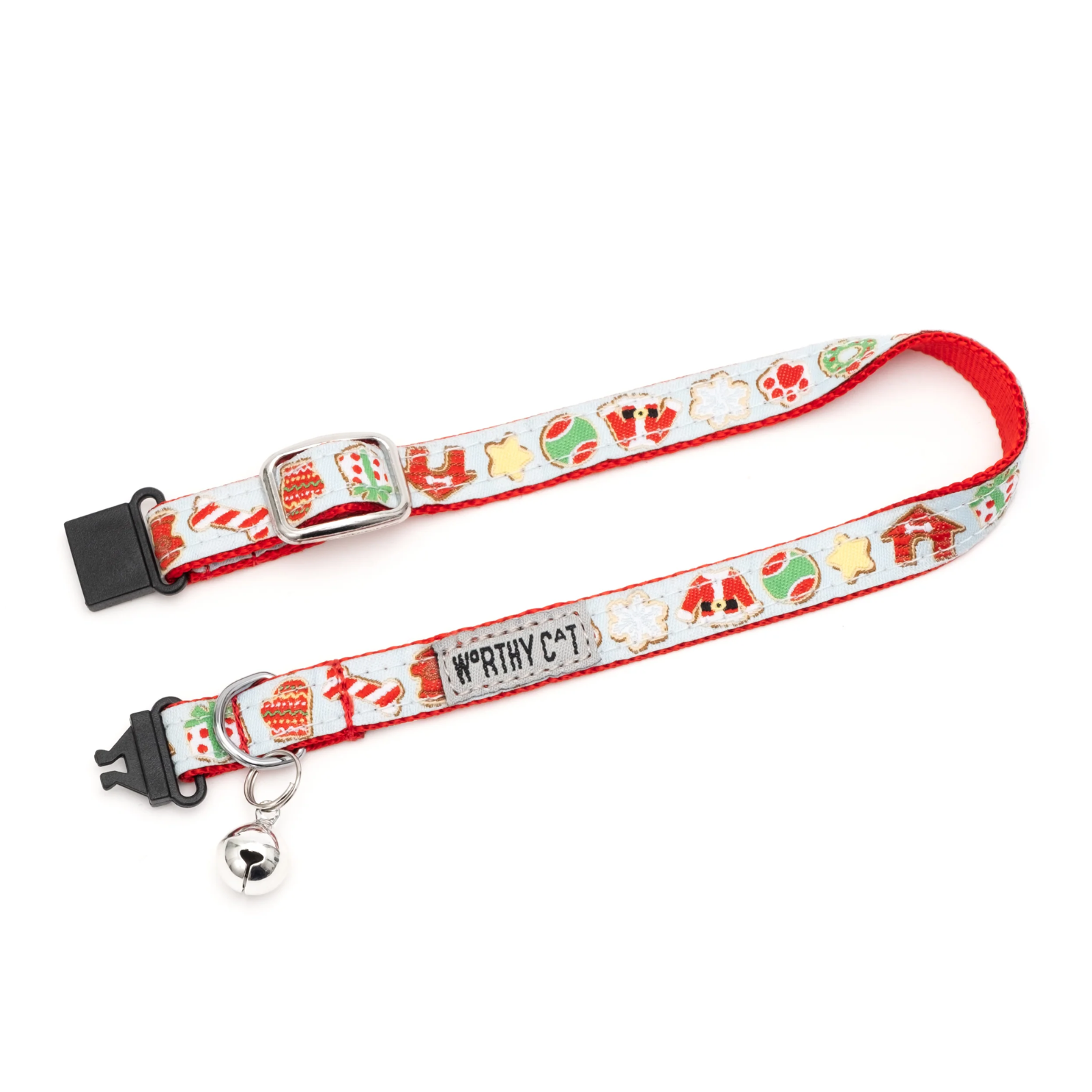 A festive Christmas-themed pet collar with a white base, red trim, and holiday illustrations including candy canes, snow globes, Santa Claus, and a bell. It features a silver metal buckle, a silver D-ring, and a small silver bell.