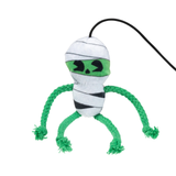 A plush dog toy shaped like a mummy, featuring white and black striped fabric body wraps, a bright green eye band with black stitched eyes and nose, and four green braided rope legs ending in frayed tips. A black hanging loop is attached at the top.