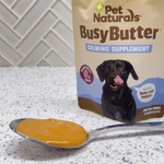 Pet Naturals Busy Butter calming supplement with a spoonful of yellow supplement on a countertop.