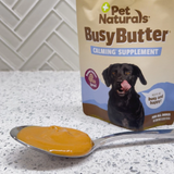 Pet Naturals Busy Butter calming supplement with a spoonful of yellow supplement on a countertop.