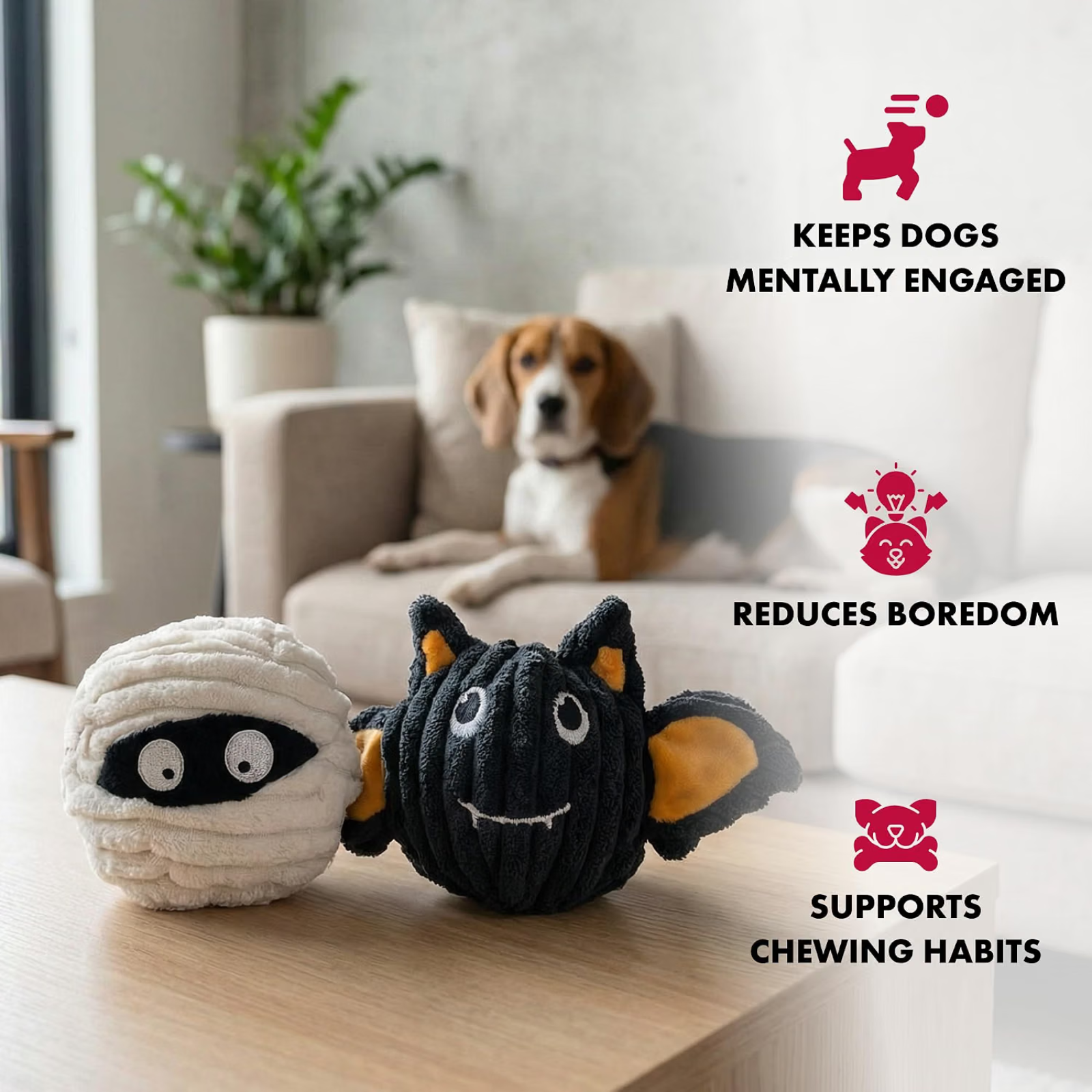 Two dog toys, one mummy-like and one bat-shaped, on a table with a dog sitting on a couch in the background.