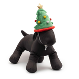 A black plush dog toy wearing a green Christmas tree hat with red trim, yellow and white pom-poms, and a gold star on top, photographed on a clean white background.