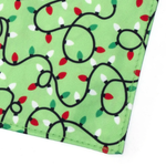 A close-up of a green fabric item, likely a pocket square or small pouch corner, featuring a printed holiday string lights pattern with black wire outlines and red, green, and white lights.