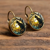 Pair of earrings with cat and moon design on a wooden surface