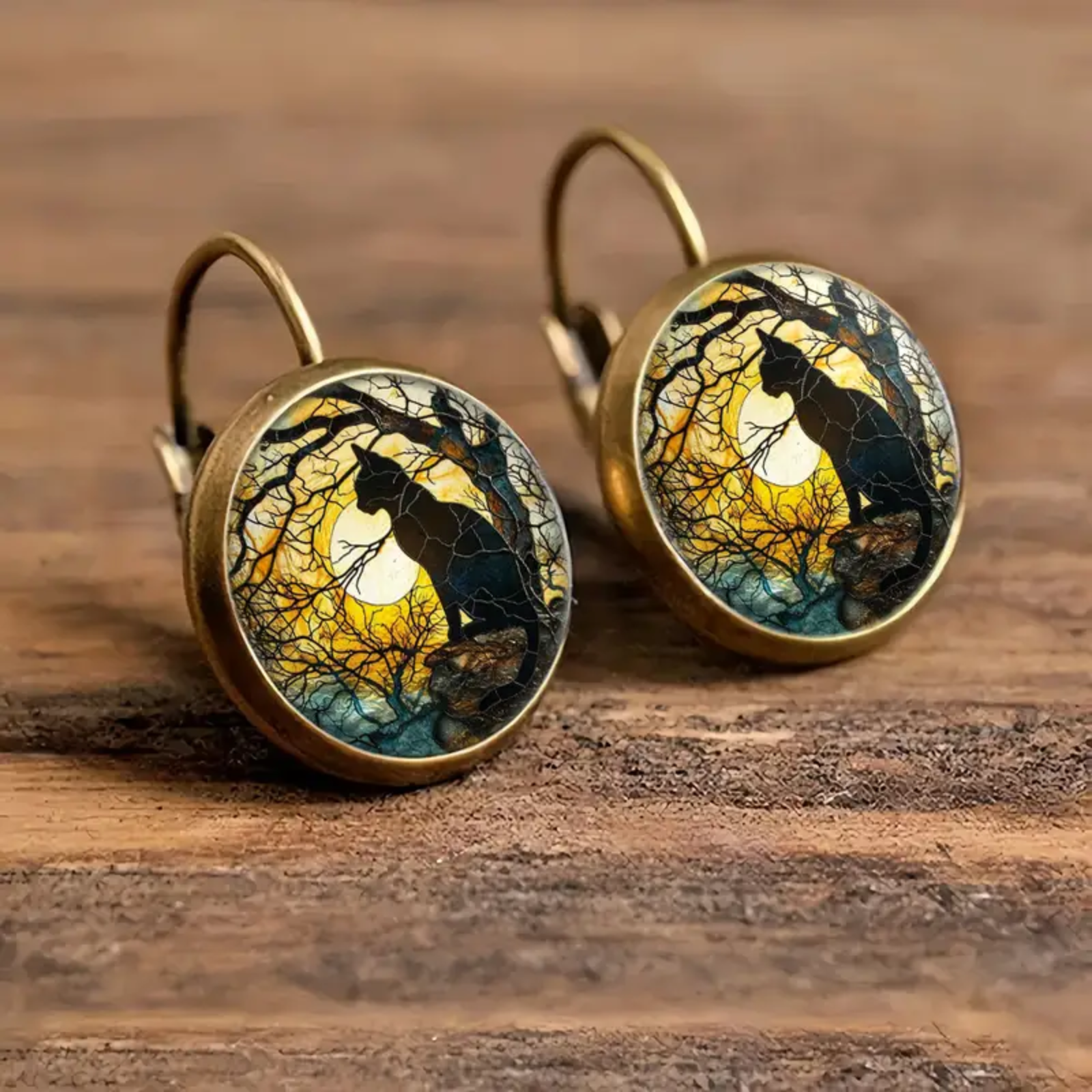 Pair of earrings with cat and moon design on a wooden surface