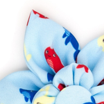 A close-up of a light blue fabric hair bow with a playful pattern of cartoon fish in red, blue, and yellow, set against a plain white background.