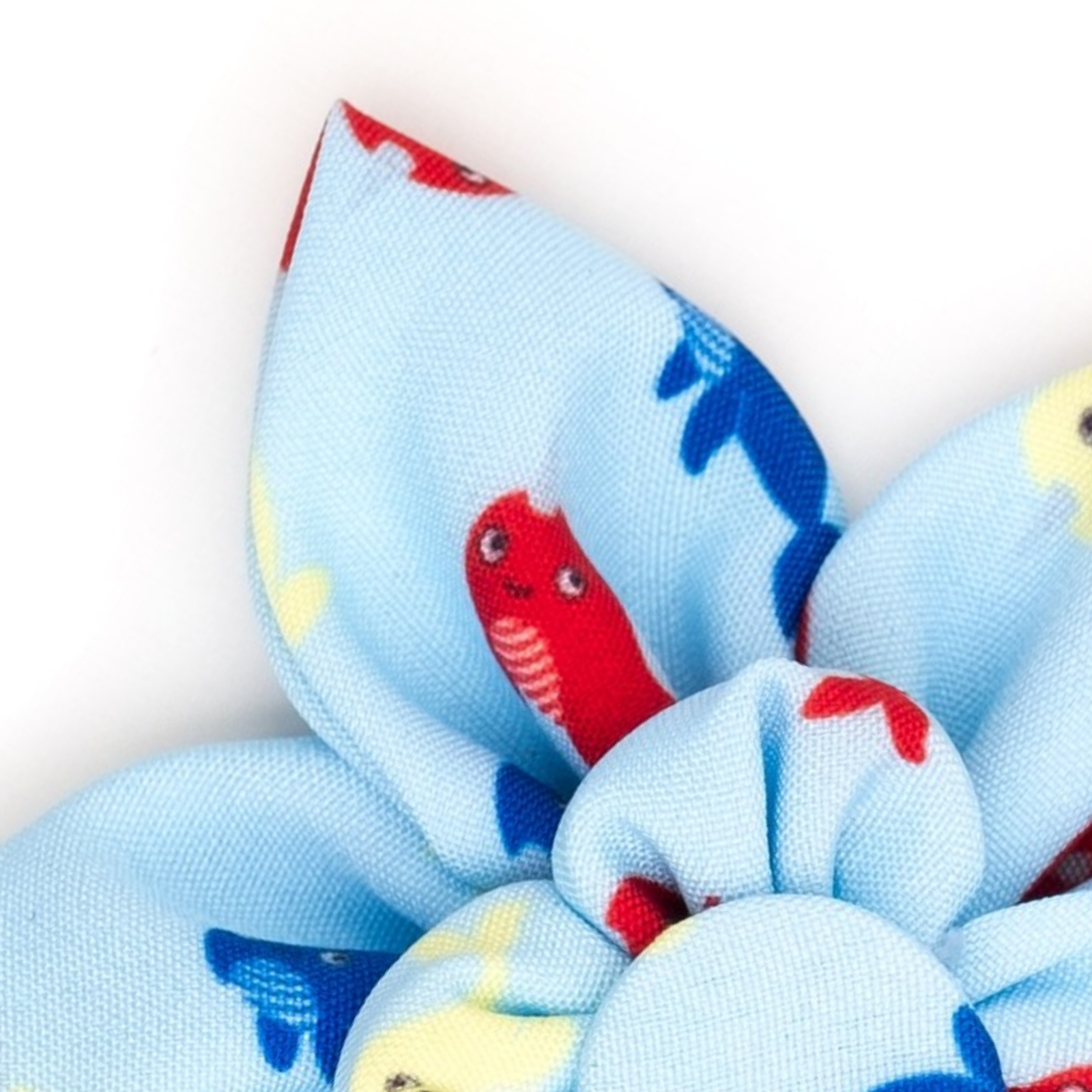 A close-up of a light blue fabric hair bow with a playful pattern of cartoon fish in red, blue, and yellow, set against a plain white background.