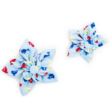 Two fabric flower hair clips in light blue with a red, blue, and yellow whale print, displayed on a clean white background.