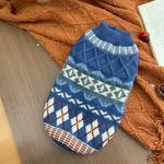 Blue patterned dog sweater on a wooden surface with a brown textured blanket in the background.