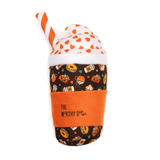 A plush dog toy shaped like a milk coffee cup with a Halloween-themed patterned body, white polka-dot lid, orange heart pattern, orange fabric sleeve, and orange-and-white striped straw. The sleeve reads 'THE WORTHY DOG'.
