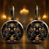 Pair of earrings with intricate designs of a black cat and coffee cup on a dark background.