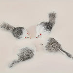 Four toy mouse-shaped cat toys made of rabbit fur in gray, white, and black, with small red eyes and red noses, arranged on a plain light background.