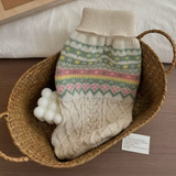 Knitted hot water bottle with a patterned cover in a woven basket on a wooden surface.
