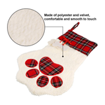 A plush pet stocking with a white faux-fur body, red tartan paw-print design, and red tartan cuff, shown on a white background with a circular fabric close-up and text noting polyester and velvet material.