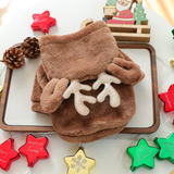 A plush brown pet hood with matching mittens featuring glittery cream reindeer antlers, styled on a wooden tray with Christmas decorations.