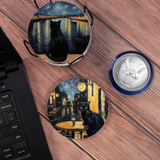 Two round coasters with black cat designs on a wooden surface next to a laptop.