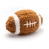 A plush football-shaped dog toy made of textured brown fleece with white stripes and white embroidered laces, photographed on a clean white background.