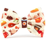 A novelty bow tie featuring a cozy autumn holiday pattern with illustrations of coffee cups, hot cocoa, cinnamon pastries, and hearts on a cream polka-dot background.