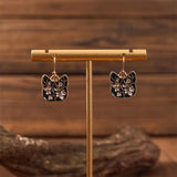 Cat-shaped earrings on a gold stand with a wooden background