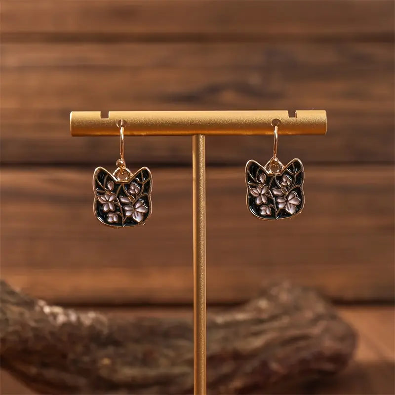 Cat-shaped earrings on a gold stand with a wooden background