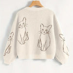 Beige sweater with cat illustrations on a hanger against a white background
