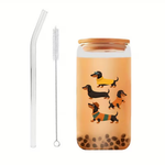 A clear glass jar with a light brown wooden lid, decorated with cartoon dachshund illustrations and filled with (bubble tea) showing dark brown pearls at the bottom. It is shown with a clear bent glass straw and a long metal cleaning brush on a plain white background.