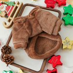 A plush brown fleece pajama set for pets, featuring a hooded sweatshirt and matching pants, arranged on a wooden tray with Christmas-themed decorative props.